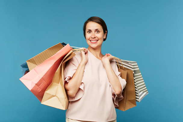 Красивая молодая улыбающаяся женщина-покупатель с кучей бумажных мешков, выражающих волнение после приятных покупок
 - Фото, изображение