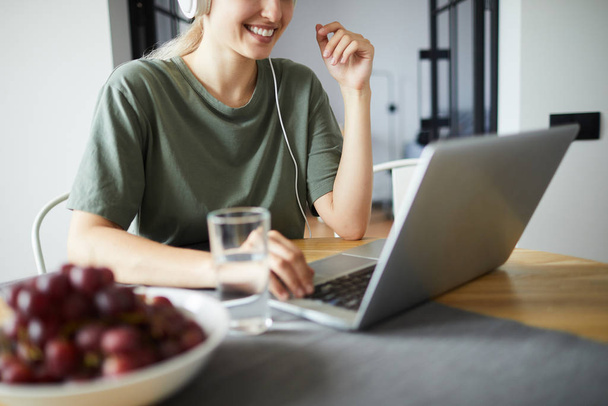 Усміхнена молода жінка сидить за столом перед ноутбуком, спілкується або взаємодіє у відео-чаті
 - Фото, зображення