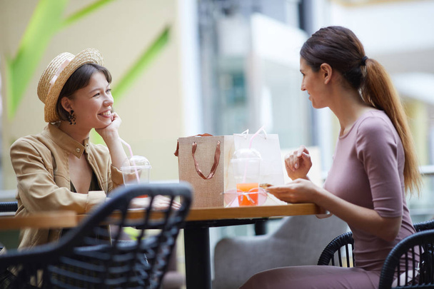 Щасливі модні молоді леді сидять за круглим столом на продовольчому корті і обговорюють продажі під час обіду
 - Фото, зображення