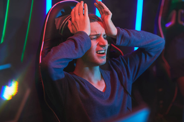 Smutný zmatený mladý původnímu hráče v šedém svetru, který držel hlavu v ruce, zatímco byl zničený ztrátou videohry - Fotografie, Obrázek