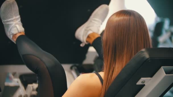 Spor salonunda egzersiz yapan sportif bir kadın - antrenman cihazına bacak presi yapmak - Video, Çekim
