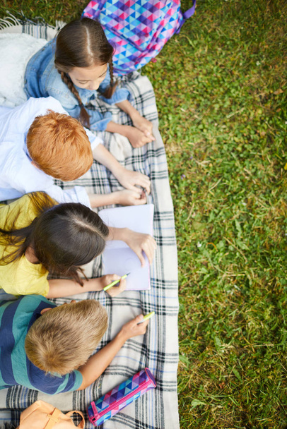 Чотири друзі підліткових шкіл роблять домашнє завдання математики разом у парку, що лежить на траві після уроків у школі
 - Фото, зображення