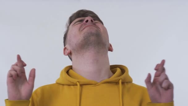 Half-length portrait of a man wearing yellow sweatshirt standing crossing his fingers with closed eyes wanted to make his wishes come true. Isolated on white. Problem skin and acne. - Felvétel, videó