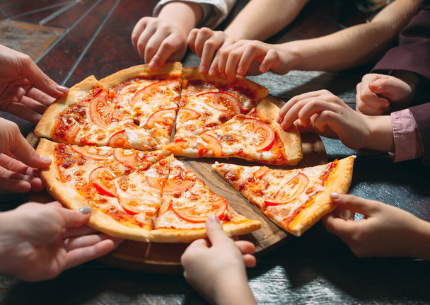 Manos tomando rebanadas de pizza de mesa de madera, vista de cerca
. - Foto, Imagen