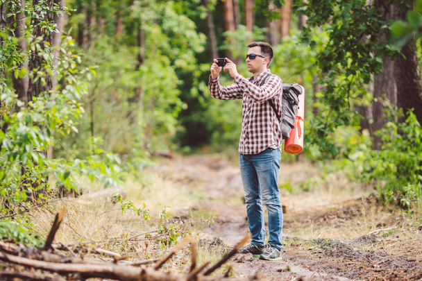 Hombre excursionista tomando foto teléfono inteligente en el bosque. Atractivo viajero haciendo foto con teléfono móvil. Caminante caminante hombre con mochila senderismo en la naturaleza, mochilero turista utilizar la cámara. concepto de vacaciones
 - Foto, Imagen