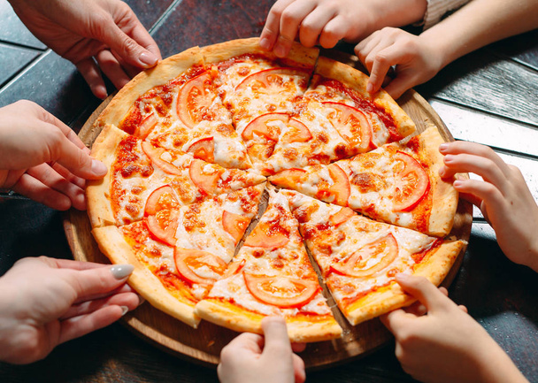 Hands taking pizza slices from wooden table, close up view. - Fotoğraf, Görsel