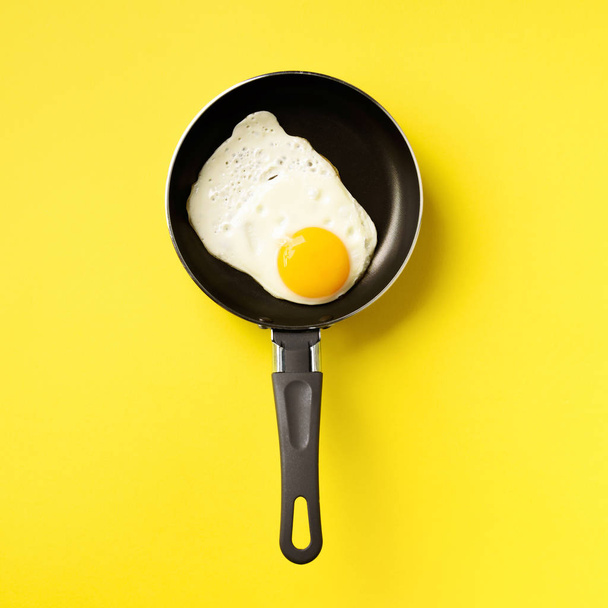 Creative food concept with fried egg on pan over yellow background. Top view. Creative pattern in minimal style. Flat lay. Square crop - Photo, image