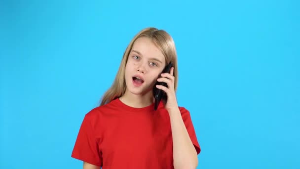 Little female talking on the phone at blue background - Кадри, відео