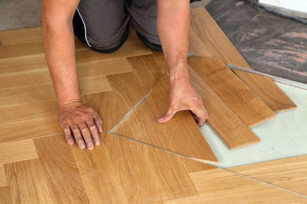 労働者は、寄せ木張りの床を敷設します。木製の積層のフロアー リングを取付けるワーカー - 写真・画像