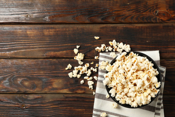 Towel and bowl with popcorn on wooden background, copy space - Foto, imagen