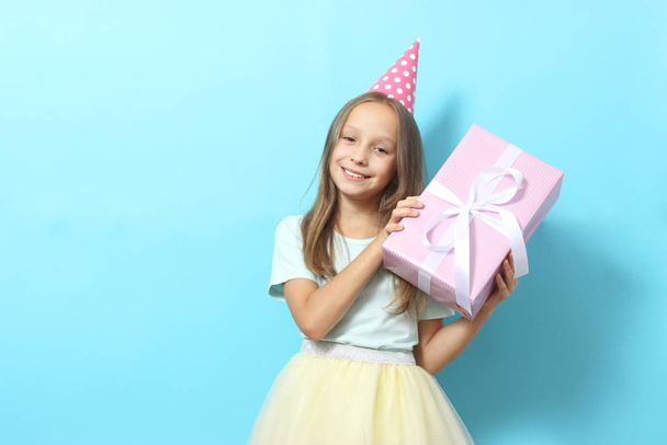 Retrato de una niña en un gorro festivo y con un regalo en sus manos en un fondo coloreado. Nacimiento, regalos, vacaciones - Foto, Imagen