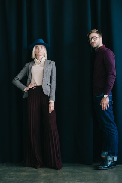full length view of stylish young man in glasses and blonde woman in hat near curtain - Valokuva, kuva