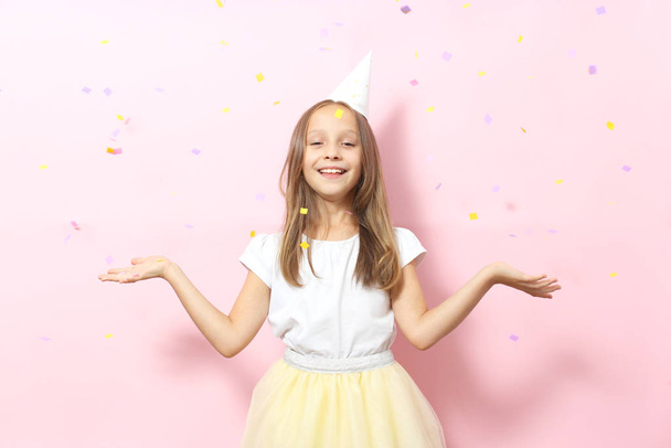 Портрет маленькой девочки в праздничной шапочке и с подарком в руках на цветном фоне. День рождения, подарки, праздник - Фото, изображение