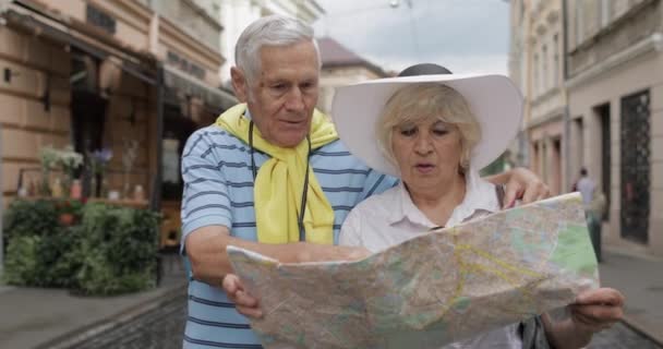 Turistas senior masculinos y femeninos de pie con un mapa en las manos buscando ruta
 - Imágenes, Vídeo