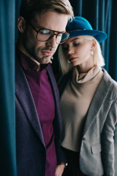 stylish young man in glasses and blonde woman in hat near curtain - Фото, зображення