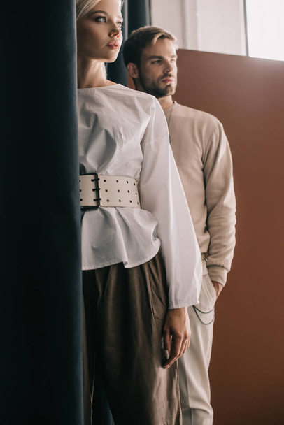 стильна молода жінка в блузці і чоловік, що стоїть біля завіси на коричневому
 - Фото, зображення