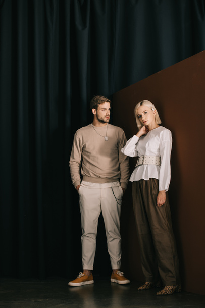 full length view of stylish man with hands in pockets and blonde woman in blouse standing near curtain - Foto, Imagen
