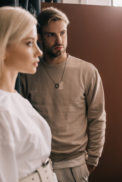 selective focus of attractive blonde girl and bearded young man with hand in pocket on brown - Foto, afbeelding