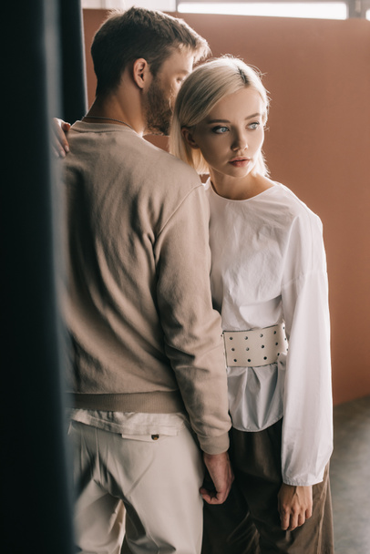stylish couple standing near curtain and looking away on brown - Photo, Image