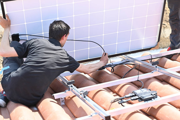 Bauarbeiter installieren Elektrokabel für die Installation von Solarzellen auf dem Dach eines Wohnhauses - Foto, Bild