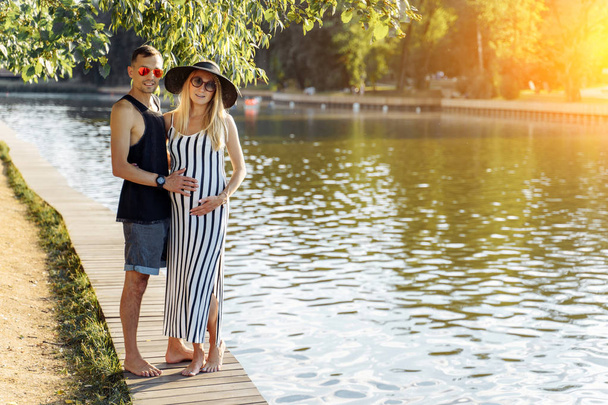 Photo of pregnant woman in hat and man standing on riverbank - Fotoğraf, Görsel