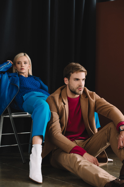 stylish blonde girl in blue leather jacket sitting on chair near man in brown coat - Photo, Image