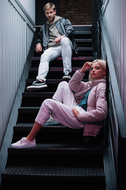 Stylische junge Männer und Frauen in lässigen Herbst-Outfits sitzen auf Treppen und schauen in die Kamera - Foto, Bild