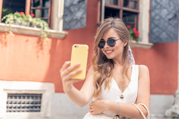 Young girl take selfie from hands with phone on summer city street - Φωτογραφία, εικόνα