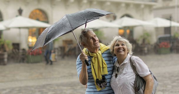 Щасливі старші туристи стоять в центрі міста і насолоджуватися дощовою погодою у Львові - Фото, зображення