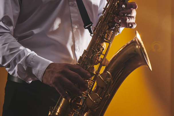 Portrait of professional musician saxophonist man in  white shirt plays jazz music on saxophone, yellow background in a photo studio, side view - Fotó, kép