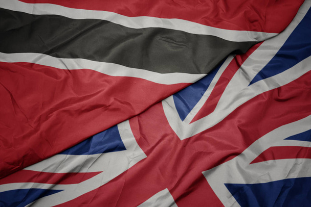 размахивая красочным флагом Великобритании и национальным флагом Тринидада и Табаго
. - Фото, изображение