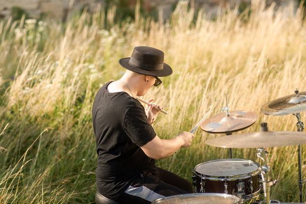 El baterista de sombrero negro ensaya al aire libre. Toca la batería en la hierba cerca del viejo castillo.
 - Foto, imagen