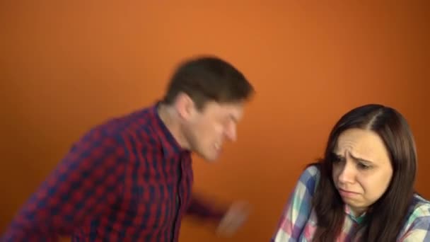 Een gekke en agressieve man schreeuwt tegen een bange jonge vrouw op een oranje achtergrond. Het concept van het stoppen van huiselijk geweld tegen vrouwen. - Video