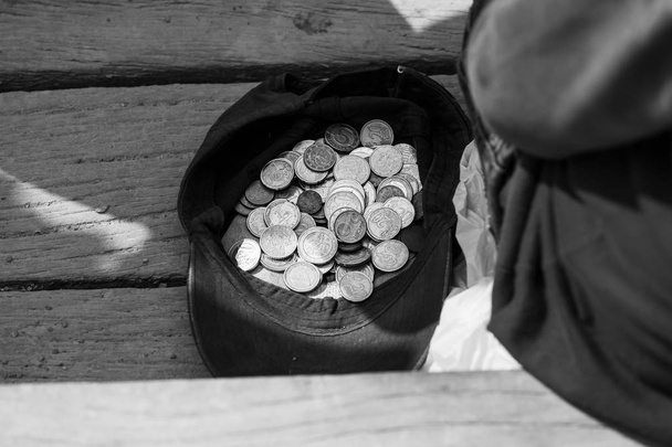 Ένας ζητιάνος κάθεται κοντά σε ένα καπάκι με κέρματα - Φωτογραφία, εικόνα