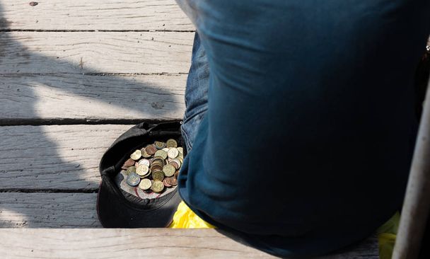 Нищий сидит у шапки с монетами
 - Фото, изображение