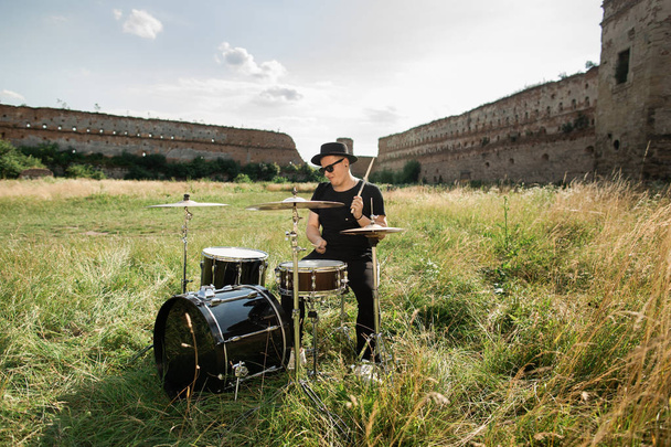 Batteur en chapeau noir répète en plein air. Il joue de la batterie dans l'herbe près du vieux château
 - Photo, image