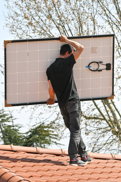 特殊工具を備えた新しい家の屋根に代替エネルギー太陽光発電パネルを設置する若い技術者 - 写真・画像