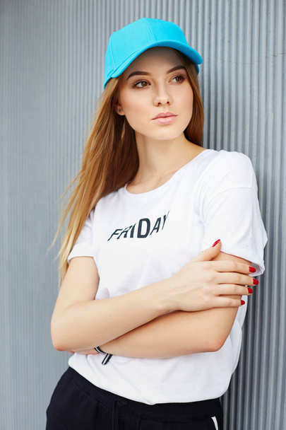 Beautiful blonde girl in a blue cap on a background of a gray wall - Photo, Image