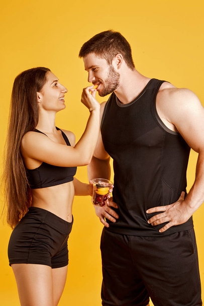 Beautiful couple of athletes with food in studio on a yellow background - Photo, Image