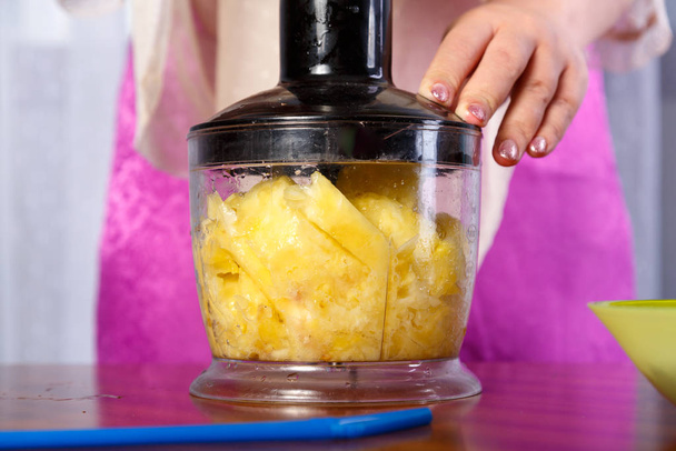 Woman chops pineapple in a blender to mash. - Fotó, kép