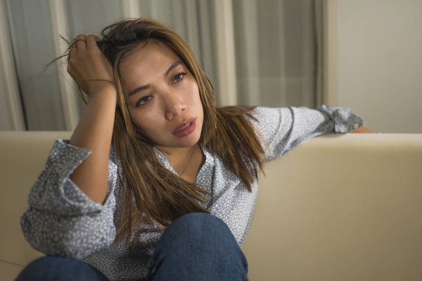 young beautiful sad and depressed Asian woman in pain thoughtful and confused at home couch feeling broken heart suffering depression crisis and anxiety problem  - Photo, image