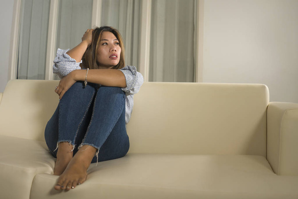 young beautiful sad and depressed Asian woman in pain thoughtful and confused at home couch feeling broken heart suffering depression crisis and anxiety problem  - Photo, image