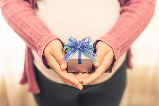 Kobieta w ciąży czuje się szczęśliwa w domu, dbając o dziecko. Młody oczekujący matka trzyma mały prezent pudełko. Macierzyństwo prenatalne opieki i kobieta koncepcja ciąży. - Zdjęcie, obraz