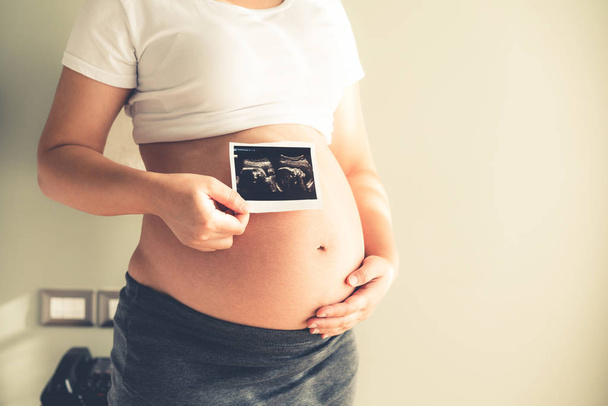 Schwangere fühlen sich zu Hause wohl, während sie sich um ihr Kind kümmern. junge werdende Mutter mit Foto. Schwangerschaftsvorsorge und Schwangerschaftskonzept für Frauen. - Foto, Bild