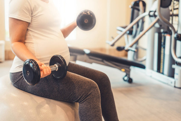 Active pregnant woman exercising in fitness center. Young expecting mother holding baby in pregnant belly. Maternity prenatal care and woman pregnancy concept. - Photo, Image
