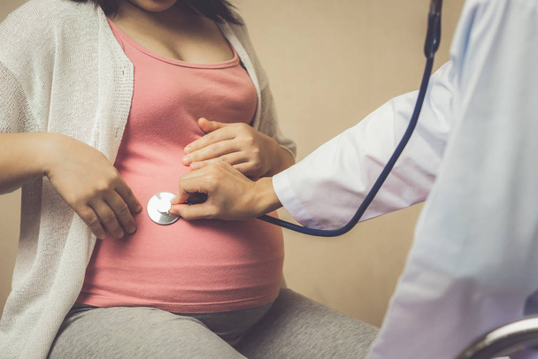 Mutlu hamile kadın gebelik konsültasyonu için hastane veya tıp kliniğinde jinekolog doktor ziyaret. Doktor bebek ve anne sağlık kontrolü için stetoskop ile hamile göbek muayene. Jinekoloji kavramı. - Fotoğraf, Görsel