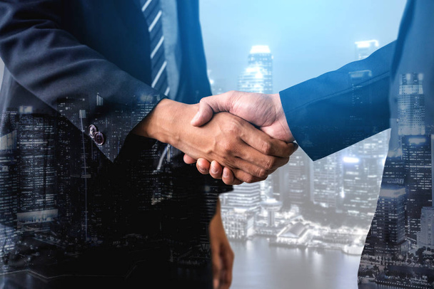 ビジネス取引のパートナーシップの成功を背景に、市役所ビルで握手するビジネスマンの二重暴露画像。企業チームワーク、トラストパートナー、労働契約の概念. - 写真・画像
