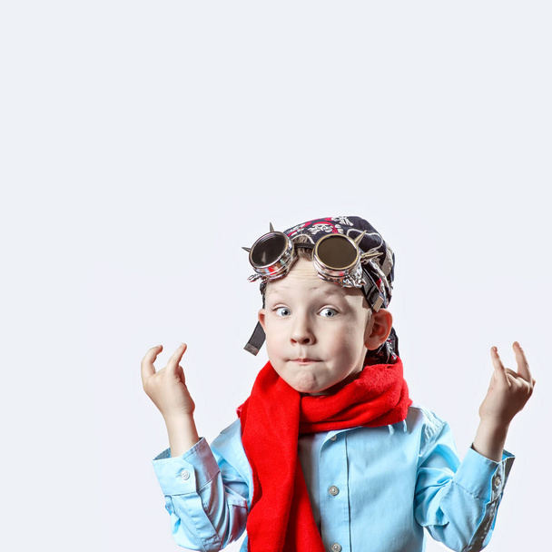 niño en camisa azul, bufanda roja, gafas de ciclista y bandana sobre fondo claro
 - Foto, Imagen