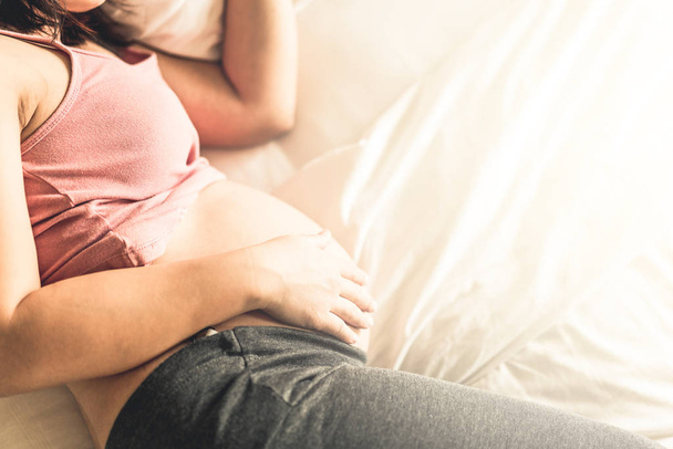 Pregnant woman feeling happy at home while taking care of child. Young expecting mother holding baby in pregnant belly. Maternity prenatal care and woman pregnancy concept. - Foto, afbeelding