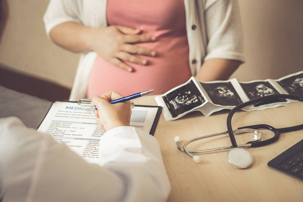 Happy pregnant woman visiting gynecologist doctor at hospital or medical clinic for pregnancy consultation. Looking at pregnancy photos. Gynecology concept. - Photo, Image